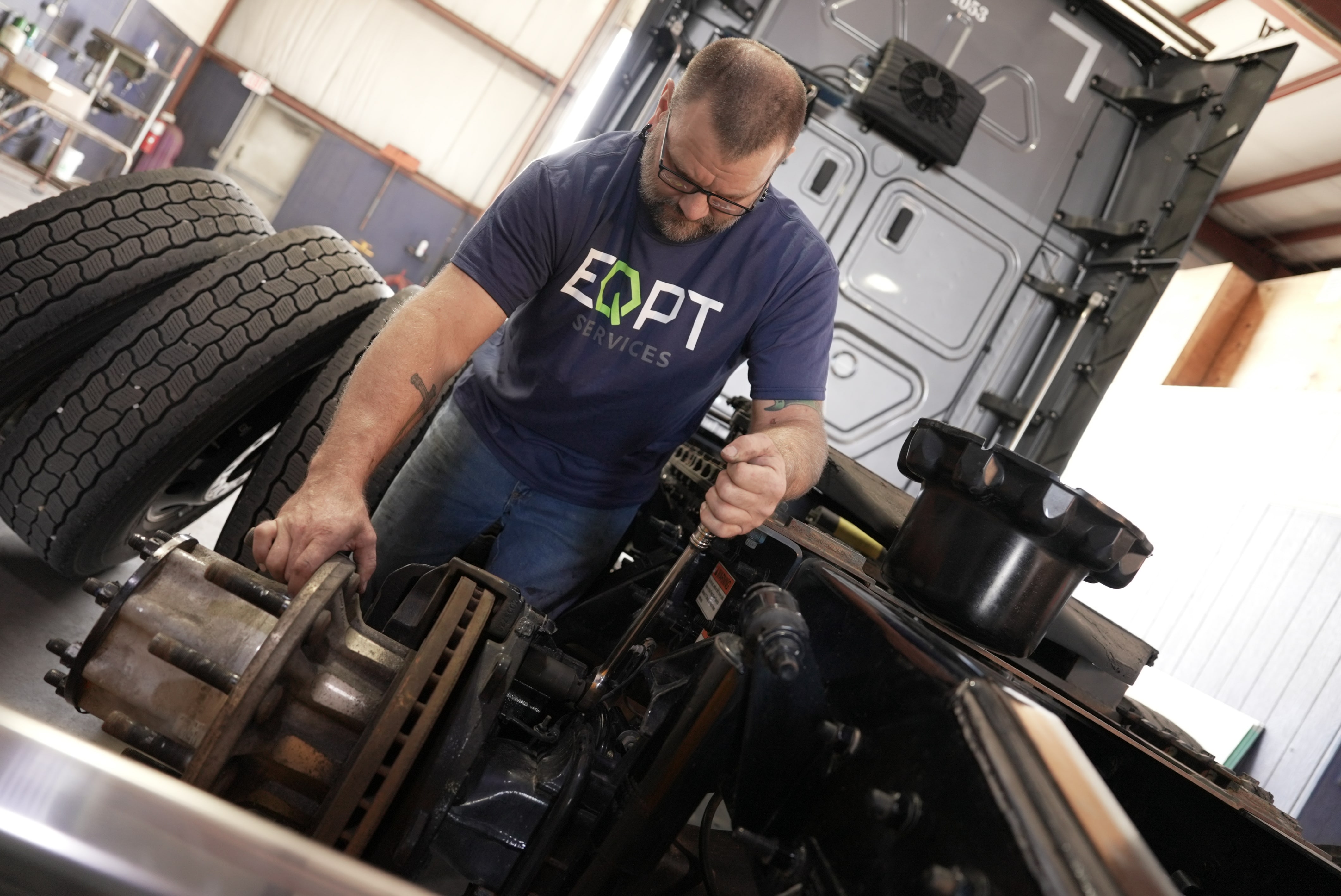 Mechanic in EQPT Services shirt working on Over-the-road (OTR) truck.